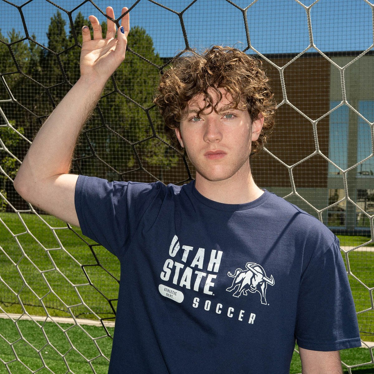 Young man wearing Utah State soccer t-shirt by soccer field fence